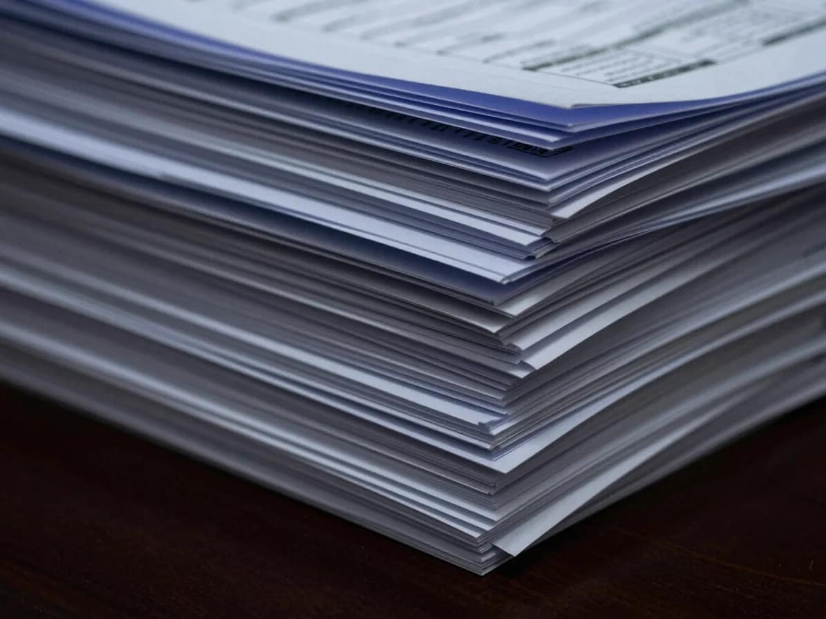 Close-up of a stack of audit documents and financial reports on a polished desk, with subtle architectural lighting from